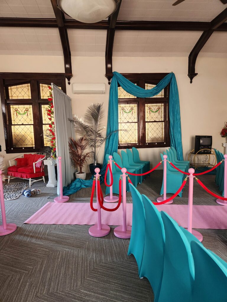 Main meeting room dressed as a film set with teal drapes, pink carpet and rope stanchions
