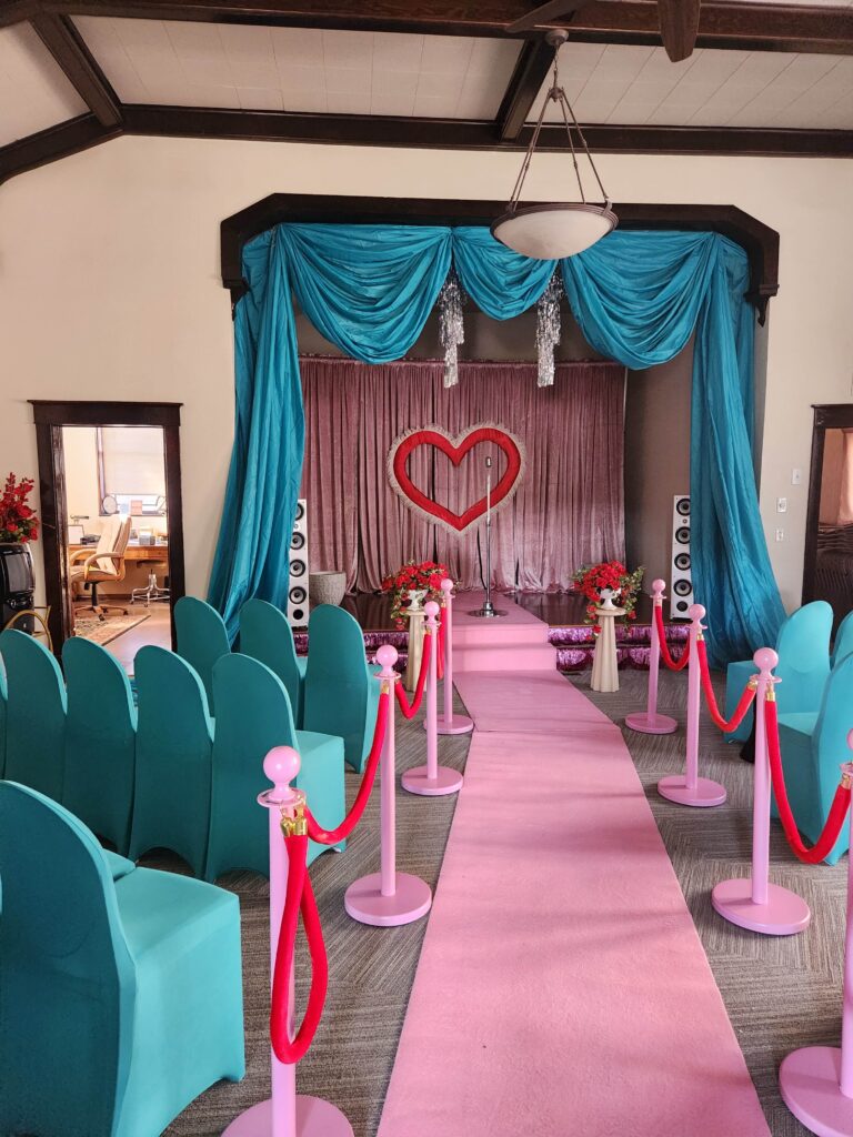 Film set in the main meeting room: a pink aisle between teal chairs leading to a stage with a heart backdrop